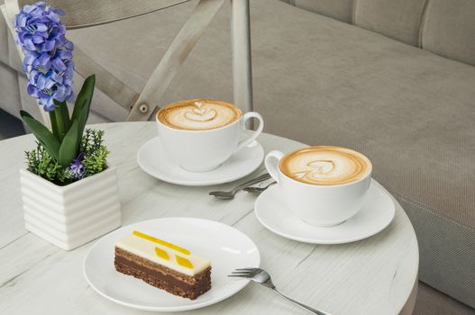 cake and two cups of coffee on a table with flowers on the background of the chair and sofa