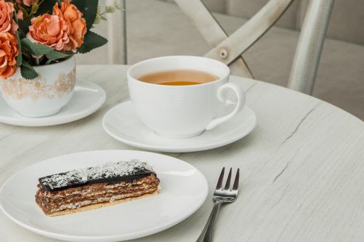 cake on a plate and a cup of coffee and fork on a table with flowers