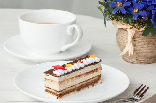 cake on a plate and a cup of coffee on a table with flowers