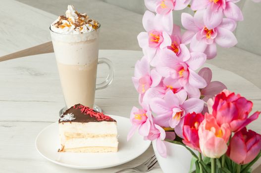 cake on a saucer and a cocktail in a tall glass on a table with flowers