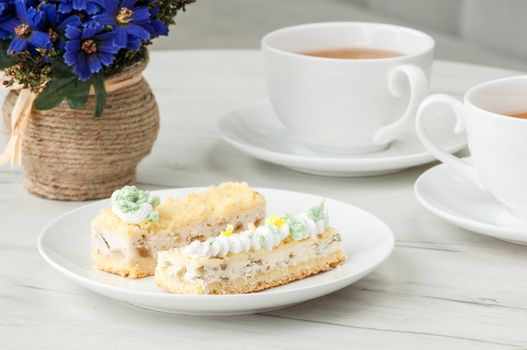 cake on a plate and two cups of tea on the table with flowers