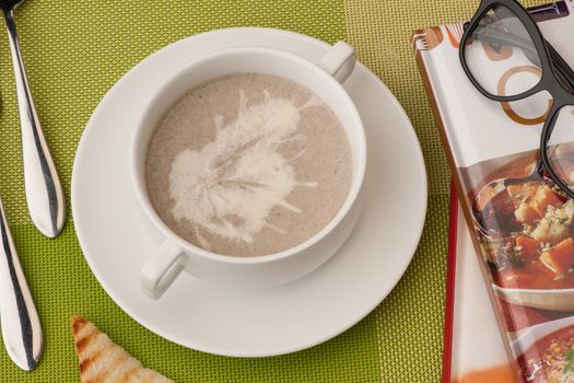 soup in a white bowl with book and glasses on a green tablecloth