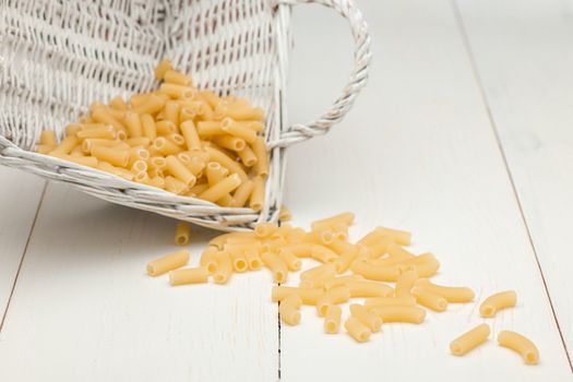 pasta in wicker basket and scattered on a white old wooden boards