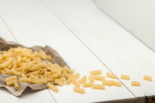 Scattered pasta in white cloth on a white old wooden boards