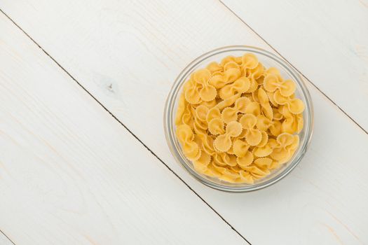 pasta in the form of glass butterflies in a transparent bowl on a white old wooden boards