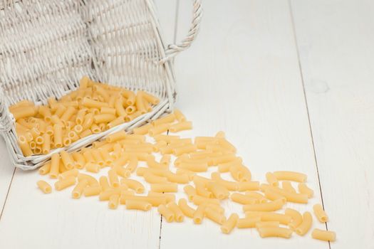 pasta in wicker basket and scattered on a white old wooden boards