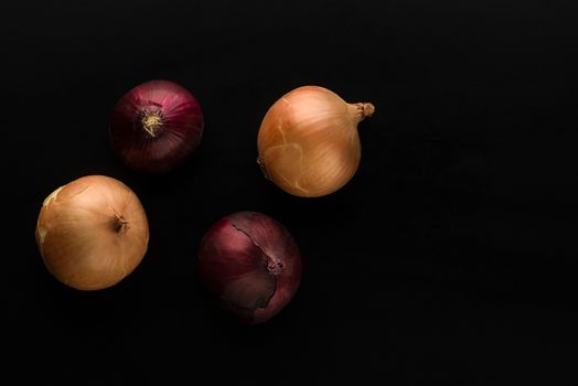 raw and unpeeled onion in red and golden colors on black background top view