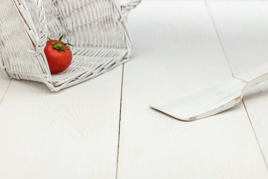 tomato in a wicker basket and a wooden spoon on a white old wooden boards