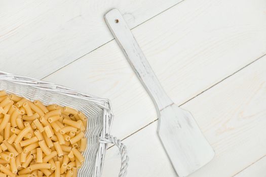 pasta in wicker basket and a wooden spoon on a white old wooden boards