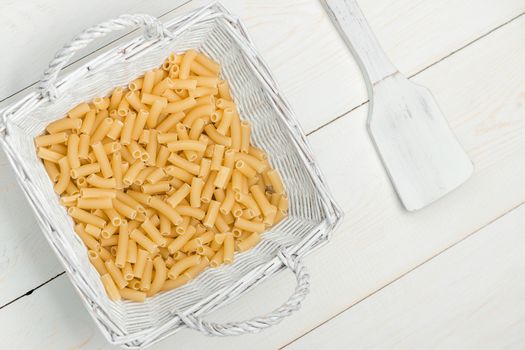 pasta in wicker basket and a wooden spoon on a white old wooden boards