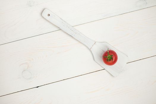 tomato on wooden spoon on white old wooden boards