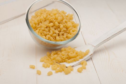 pasta in a transparent plate of glass and wooden spoon on a white old wooden boards