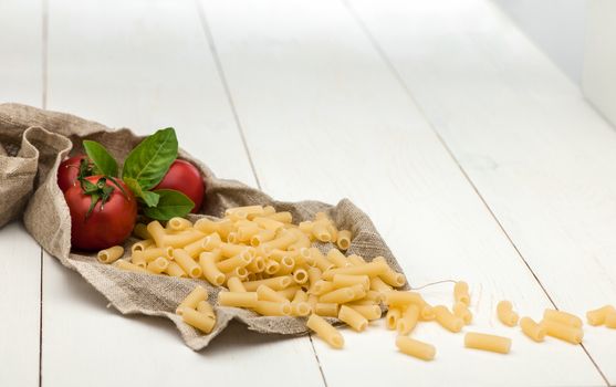 pasta and tomatoes in a tissue and scattered on a white old wooden boards