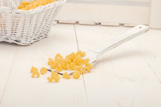 pasta in wicker basket and a wooden spoon on a white old wooden boards