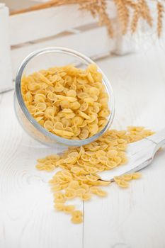 pasta in a transparent plate of glass and wooden spoon on a white old wooden boards