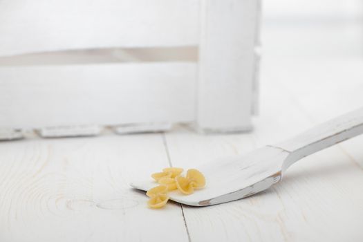 pasta on a wooden spoon and a box on a white old wooden boards