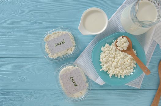 Cottage cheese in plastic packaging and milk on a wooden blue background, top view. healthy eating concept