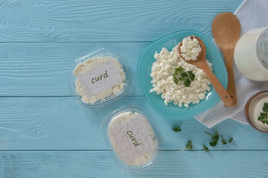 Cottage cheese in plastic packaging and milk on a wooden blue background, top view. healthy eating concept