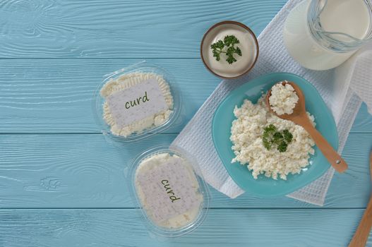 Cottage cheese in plastic packaging and milk on a wooden blue background, top view. healthy eating concept