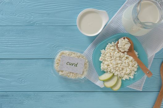 Cottage cheese in plastic packaging and milk on a wooden blue background, top view. healthy eating concept