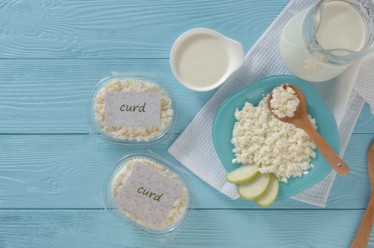 Cottage cheese in plastic packaging and milk on a wooden blue background, top view. healthy eating concept