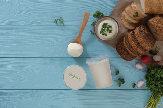 yogurt in a plastic container and bread on a blue wooden background, top view. healthy eating concept