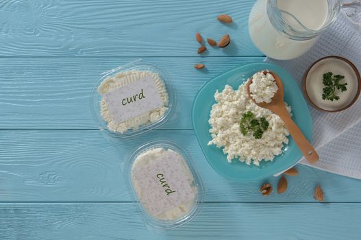 Cottage cheese in plastic packaging and milk on a wooden blue background, top view. healthy eating concept