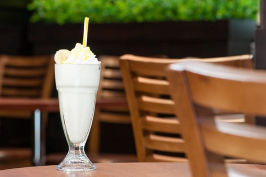 cold milkshake in a glass with a straw on a table