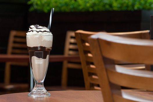 cold milk chocolate cocktail in a glass with a straw on a table