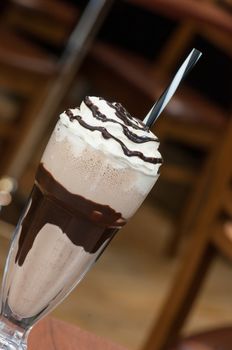 cold milk chocolate cocktail in a glass with a straw on a table