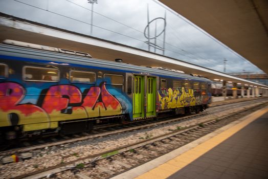 teni,italy may 28 2020 :trains panning at the station at speed with people inside and colored by graffiti