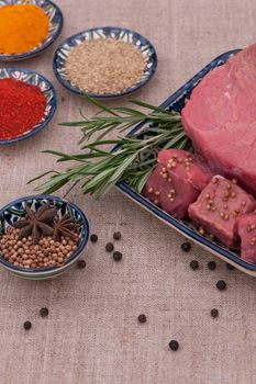 raw meat with spices and herbs in a square plate on a textured tissue