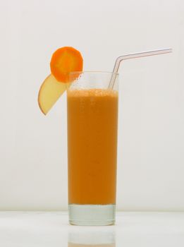 carrot juice in a glass with a straw and a slice of carrot and apple. drink isolated on white background