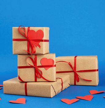 stack of wrapped gifts in brown kraft paper and tied with a red ribbon on a blue background, surprise and a gift for Valentine's Day February 14