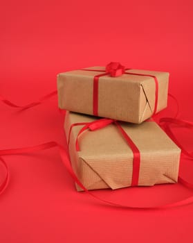 square box wrapped in brown kraft paper and tied with a red thin silk ribbon on a red background, holiday Valentine's Day.  Anniversary, birthday.