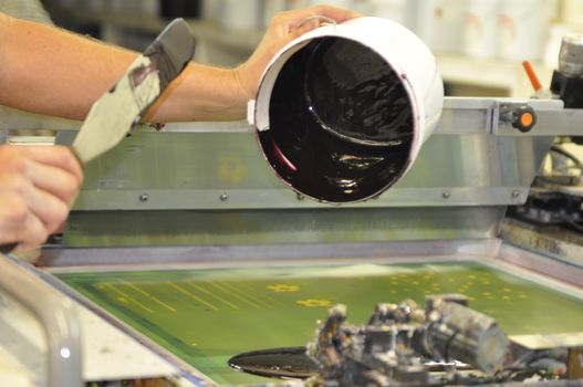 a screen printer adding some black ink to his screen, ready to print his next colour