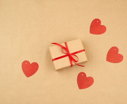 gift wrapped in brown kraft paper and tied with a thin silk ribbon on a background of paper, top view. Congratulations on Valentine's Day February 14