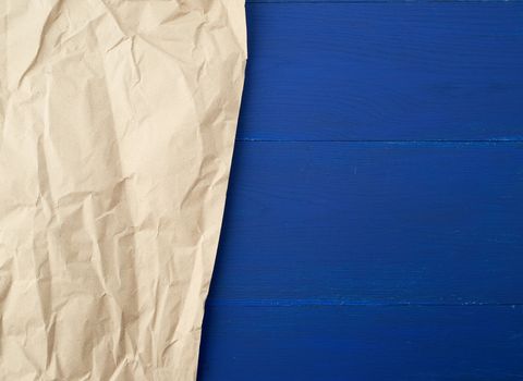 piece of crumpled blank sheet of brown wrapping paper. Grunge texture. kraft paper texture on a blue wooden background 