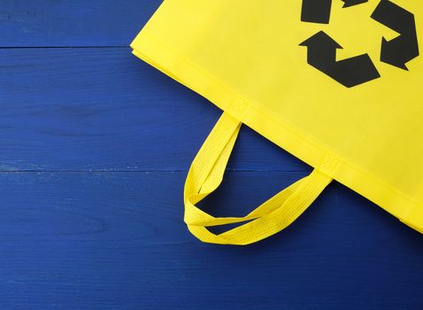 Reusable yellow viscose bag on blue wooden background, plastic waste reduction concept