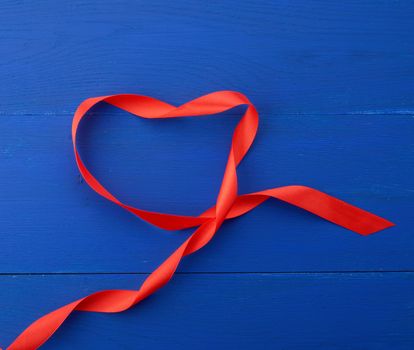 twisted silk ribbon on a blue wooden background, abstract holiday backdrop