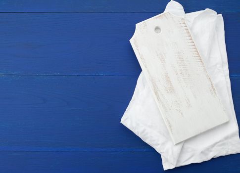 rectangular empty white kitchen cutting board and white textile towel on a blue wooden background from boards, top view