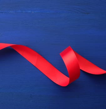 red silk thin ribbon twisted on a blue wooden background, trendy classic color, top view