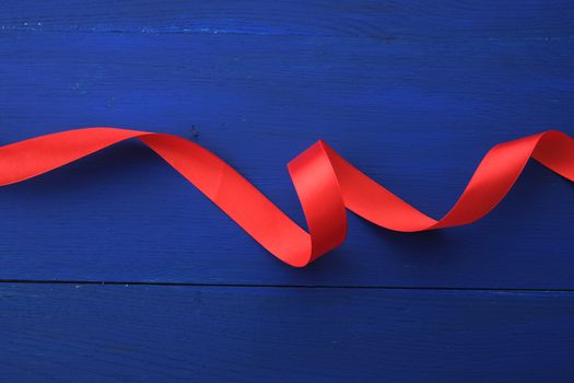 red silk thin ribbon twisted on a blue wooden background, trendy classic color, top view