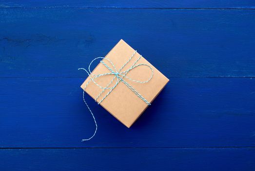 brown cardboard gift square box on a blue wooden background, top view. Festive concept, copy space