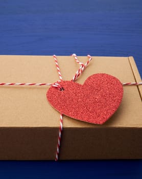 rectangular brown box with a gift and a red paper heart tied to a rope, blue wooden background, close up