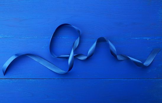 twisted silk blue ribbon on a blue wooden background, abstract holiday backdrop
