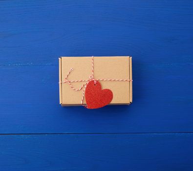 rectangular brown box with a gift and a red paper heart tied to a rope, blue wooden background, top view