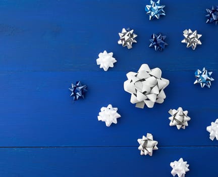 related white, blue and gray bows for gifts on a blue wooden background, decor for decorating gifts, top view