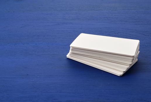 stack of white blank paper rectangular business cards on blue wooden background. Mockup with white paper card
