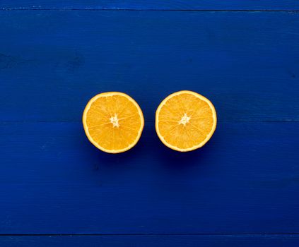 two halves of an orange round orange on a dark blue background from boards painted in blue trend color, place for an inscription